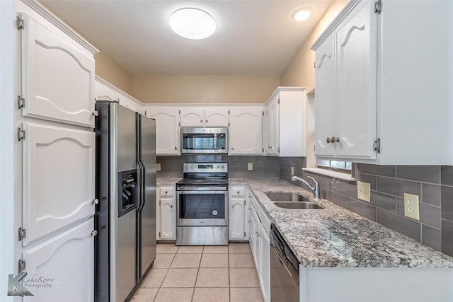 kitchen with appliances with stainless steel finishes, light stone counters, a sink, light tile patterned floors, and backsplash