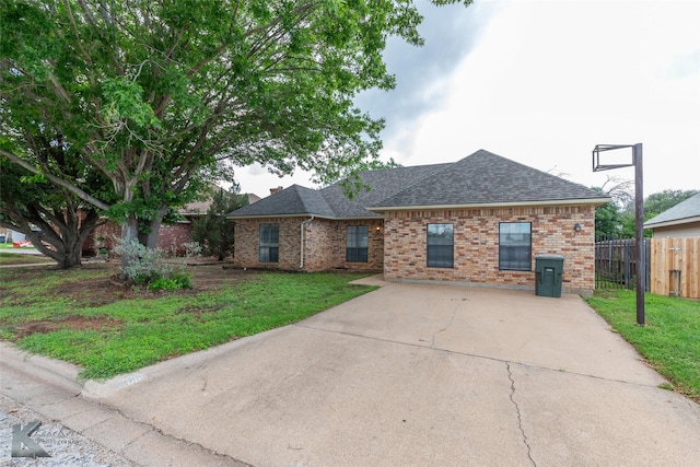 single story home with brick siding, fence, roof with shingles, and a front lawn