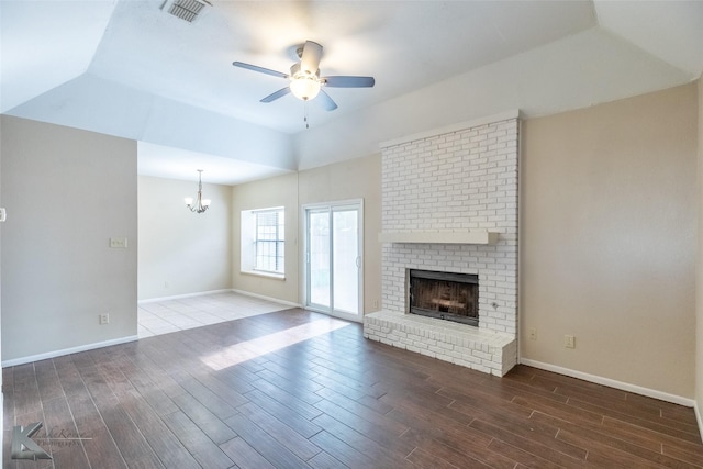 unfurnished living room featuring a brick fireplace, ceiling fan with notable chandelier, wood finished floors, and visible vents
