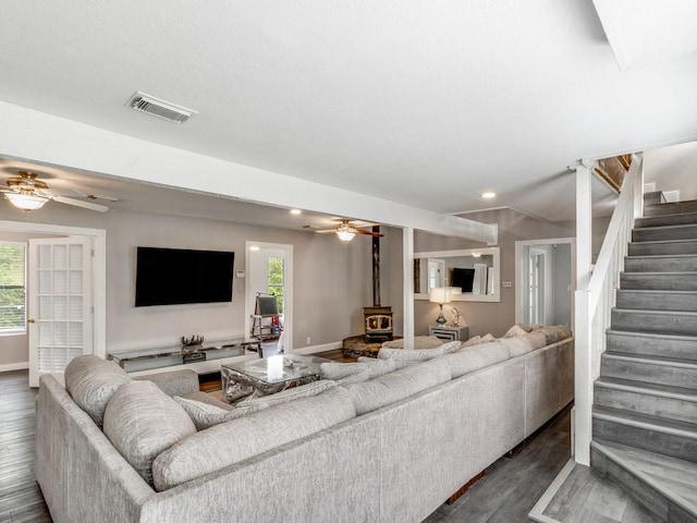 living area with a ceiling fan, stairway, visible vents, and a wood stove