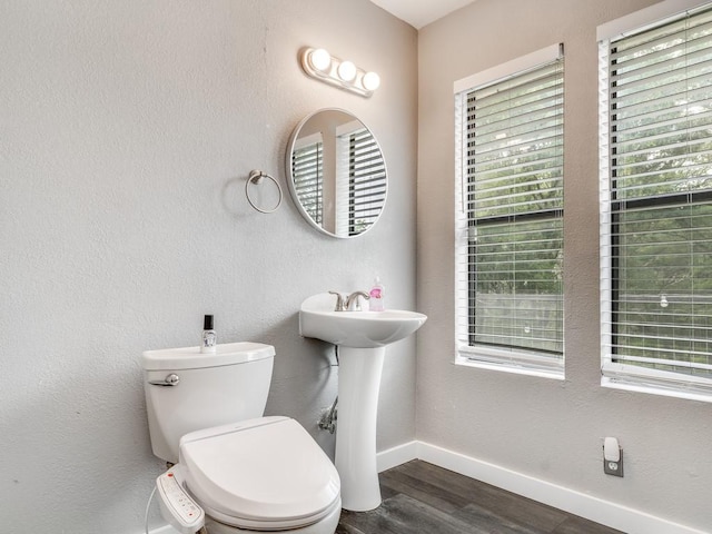 half bath with toilet, baseboards, a healthy amount of sunlight, and wood finished floors