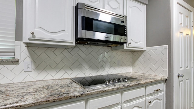 kitchen with black electric stovetop, white cabinetry, stainless steel microwave, light stone counters, and backsplash