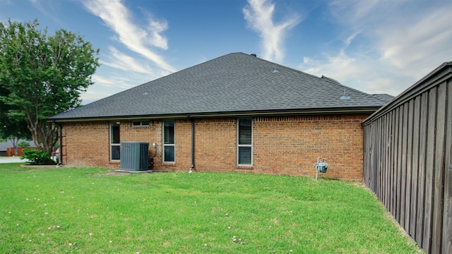 back of property featuring roof with shingles, a yard, cooling unit, and brick siding