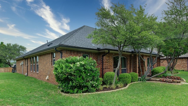 view of side of property with roof with shingles, a yard, and brick siding