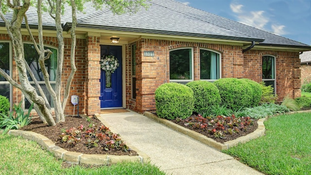 entrance to property featuring brick siding and roof with shingles