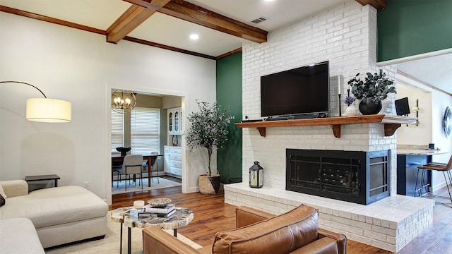 living room featuring visible vents, a fireplace, beam ceiling, wood finished floors, and an inviting chandelier