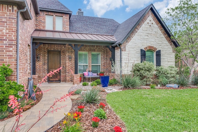 view of front of property with a standing seam roof, a shingled roof, a front lawn, and brick siding