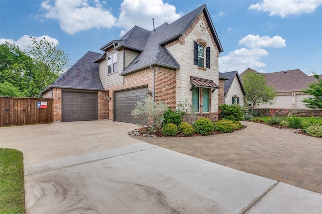 view of front of property featuring fence, stone siding, roof with shingles, brick siding, and driveway