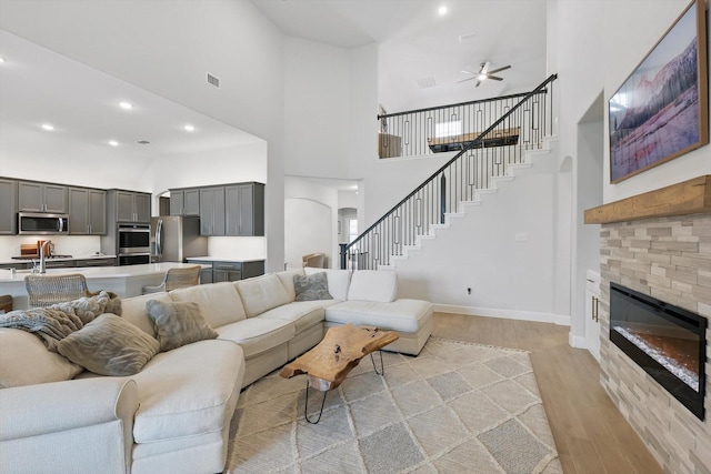 living area with a ceiling fan, visible vents, light wood-type flooring, a glass covered fireplace, and a high ceiling