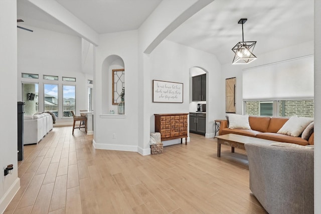 interior space featuring light wood-style floors, arched walkways, baseboards, and high vaulted ceiling
