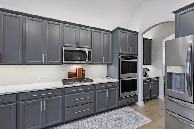 kitchen with light wood-type flooring, arched walkways, decorative backsplash, and stainless steel appliances