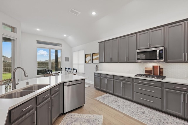 kitchen with a sink, stainless steel appliances, vaulted ceiling, tasteful backsplash, and visible vents