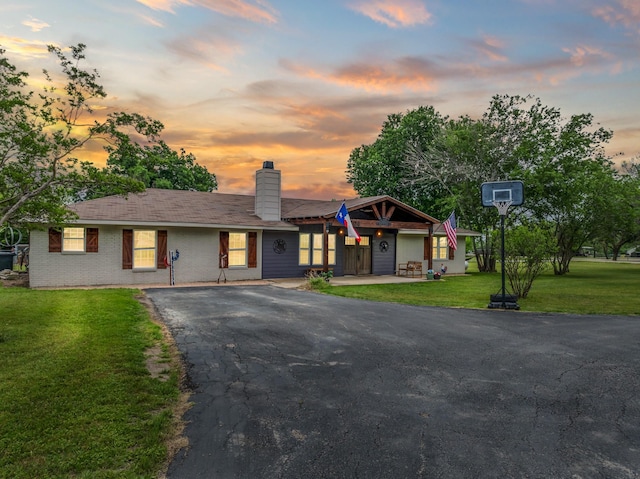 view of front of property with a lawn, a chimney, driveway, and brick siding