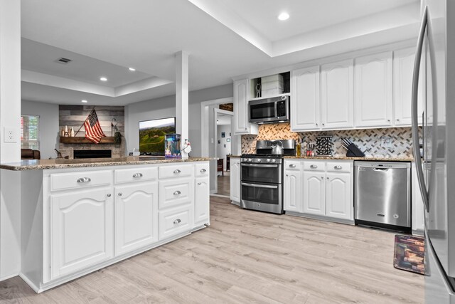 living area with a stone fireplace, visible vents, light wood finished floors, a tray ceiling, and recessed lighting