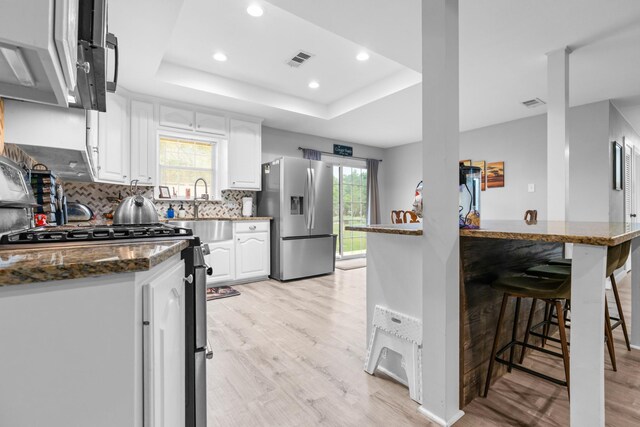 kitchen featuring backsplash, stainless steel appliances, light wood-type flooring, a tray ceiling, and recessed lighting