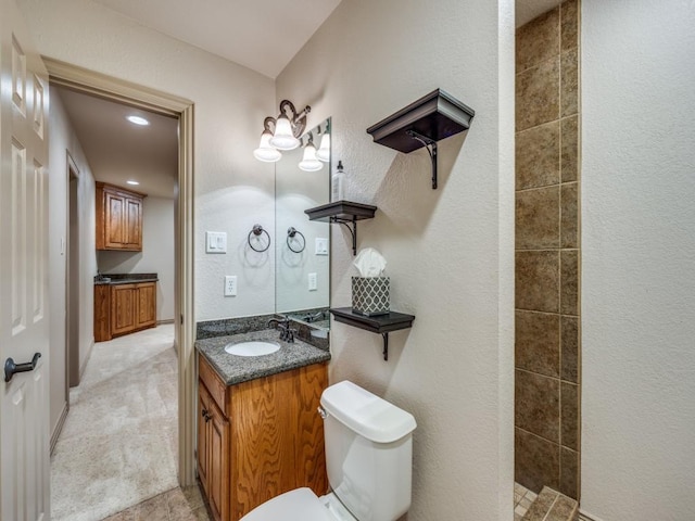 bathroom featuring a textured wall, a tile shower, vanity, toilet, and recessed lighting
