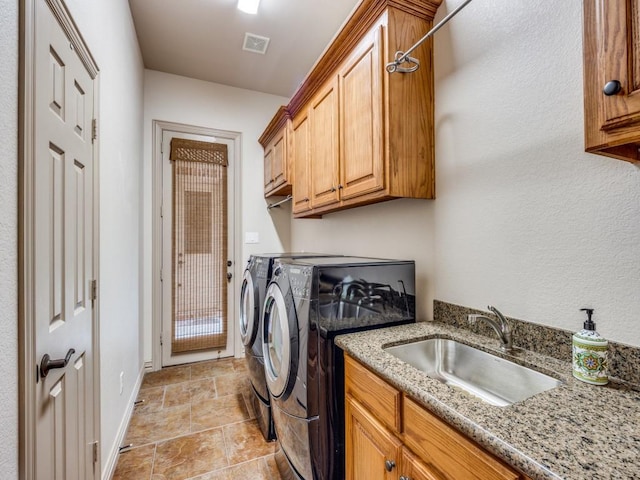 clothes washing area featuring stone finish flooring, washing machine and clothes dryer, visible vents, cabinet space, and a sink