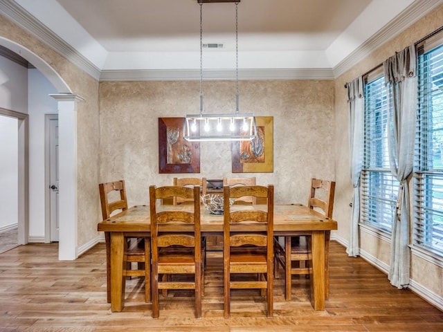 dining room featuring arched walkways, a healthy amount of sunlight, and wood finished floors