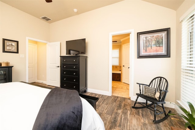 bedroom with visible vents, wood finished floors, baseboards, ensuite bathroom, and vaulted ceiling