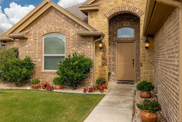 view of exterior entry featuring brick siding, a lawn, and stone siding
