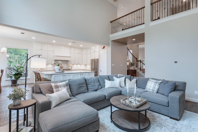 living room featuring a towering ceiling, light wood-style floors, baseboards, stairway, and recessed lighting