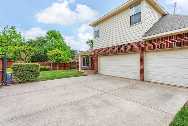 view of side of home featuring fence, brick siding, a shingled roof, concrete driveway, and a yard
