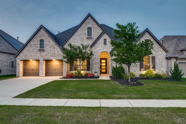 french country inspired facade with brick siding, a front lawn, an attached garage, and concrete driveway