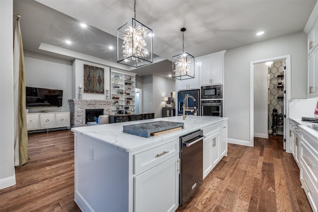 kitchen featuring a kitchen island with sink, a fireplace, dark wood-style floors, light stone counters, and stainless steel appliances
