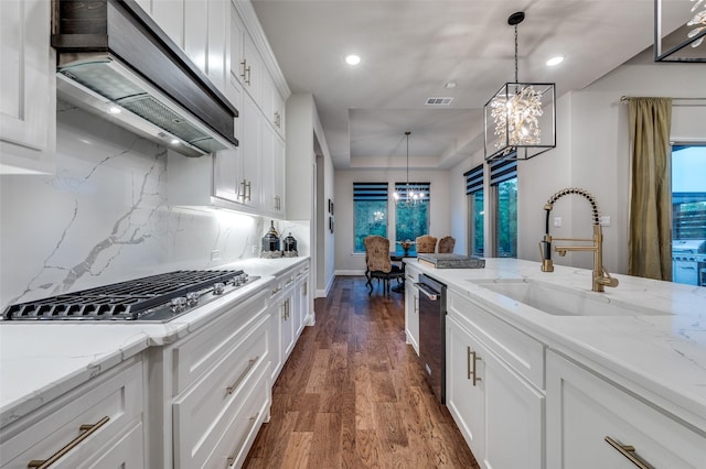 kitchen with wall chimney exhaust hood, a raised ceiling, a chandelier, a sink, and stainless steel gas stovetop