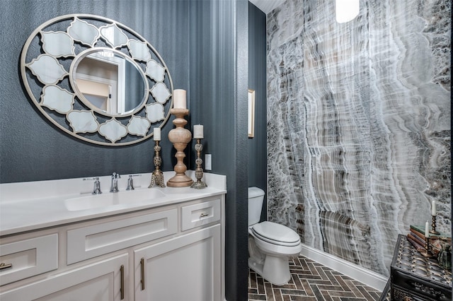 bathroom featuring vanity, brick floor, baseboards, and toilet