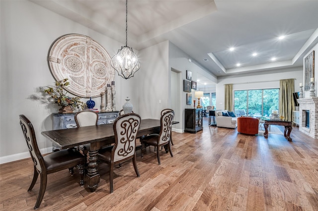 dining space featuring a brick fireplace, baseboards, light wood finished floors, a notable chandelier, and a tray ceiling