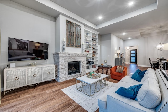 living area featuring a fireplace, wood finished floors, a raised ceiling, baseboards, and recessed lighting