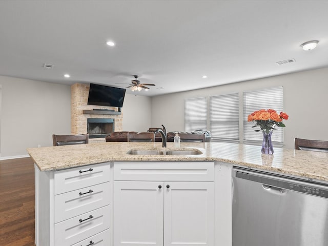 kitchen with ceiling fan, a sink, a stone fireplace, stainless steel dishwasher, and visible vents