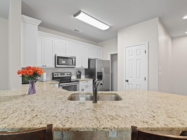 kitchen featuring visible vents, appliances with stainless steel finishes, a sink, light stone counters, and white cabinetry