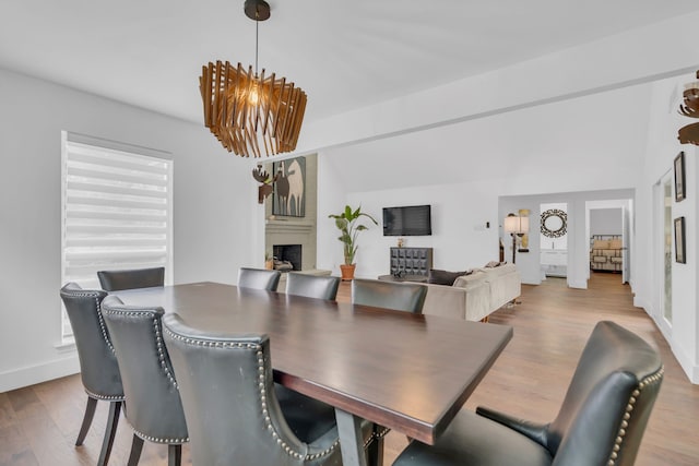 dining space featuring a fireplace, a chandelier, baseboards, wood finished floors, and vaulted ceiling