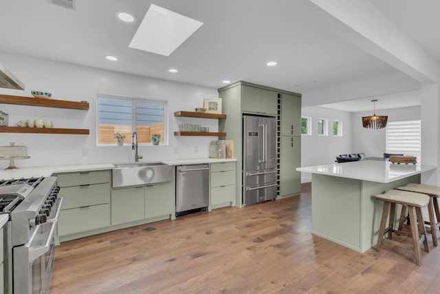 kitchen featuring high quality appliances, green cabinetry, open shelves, a sink, and a kitchen breakfast bar