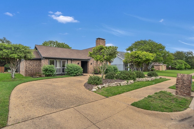ranch-style house with roof with shingles, a chimney, a front yard, and brick siding