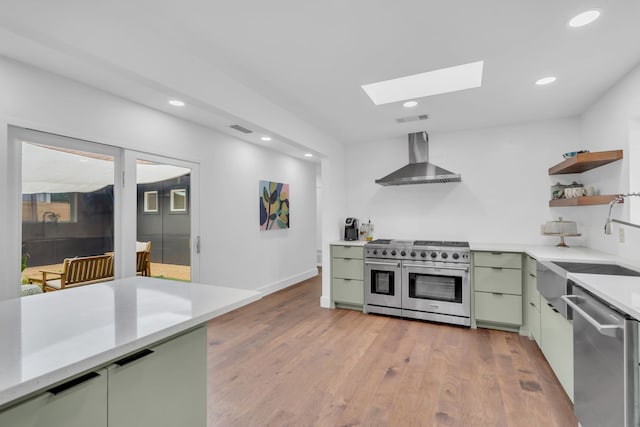kitchen featuring wall chimney range hood, a skylight, light countertops, green cabinets, and stainless steel appliances