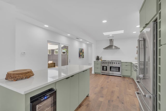 kitchen featuring wine cooler, high end appliances, wall chimney range hood, recessed lighting, and green cabinetry