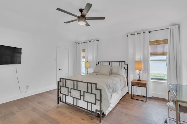 bedroom with baseboards, ceiling fan, multiple windows, and wood finished floors