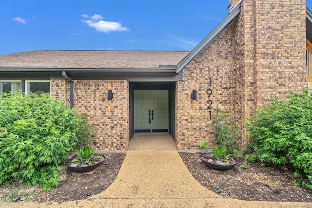 property entrance with brick siding, roof with shingles, and a chimney