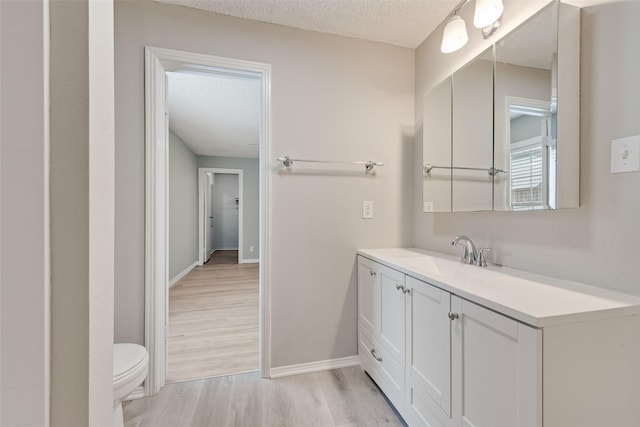 bathroom featuring a textured ceiling, wood finished floors, baseboards, vanity, and toilet