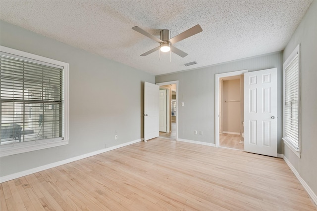 unfurnished bedroom featuring visible vents, a textured ceiling, wood finished floors, and multiple windows