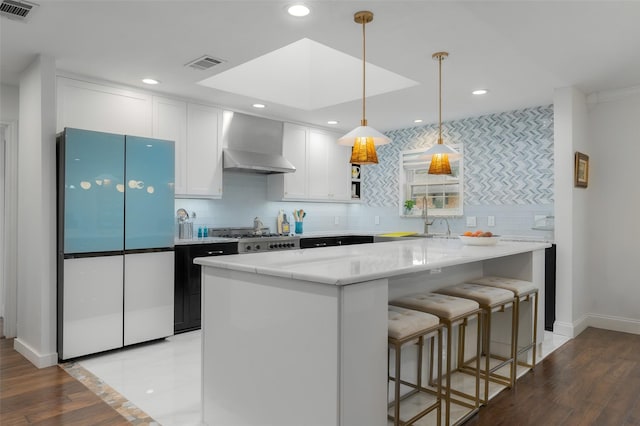 kitchen with visible vents, freestanding refrigerator, wall chimney exhaust hood, and white cabinets