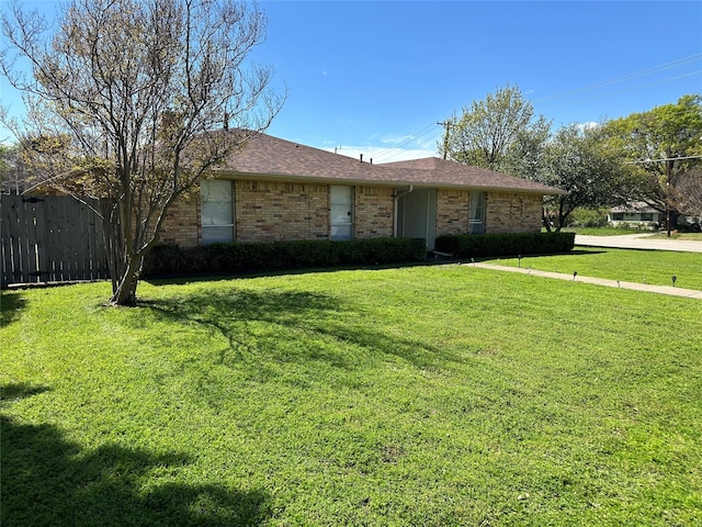 ranch-style house featuring fence, roof with shingles, a front lawn, and brick siding