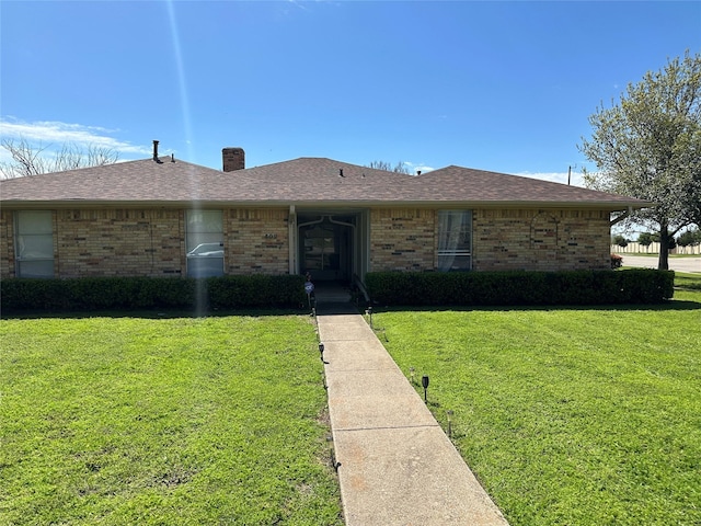 view of front of property with brick siding, a chimney, roof with shingles, and a front lawn