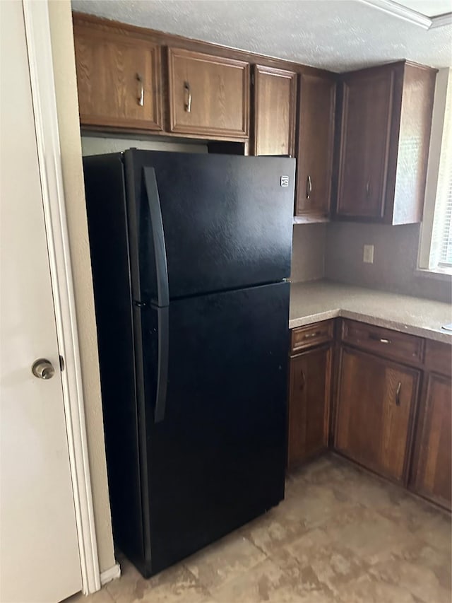 kitchen with freestanding refrigerator, a textured ceiling, dark brown cabinets, and light countertops