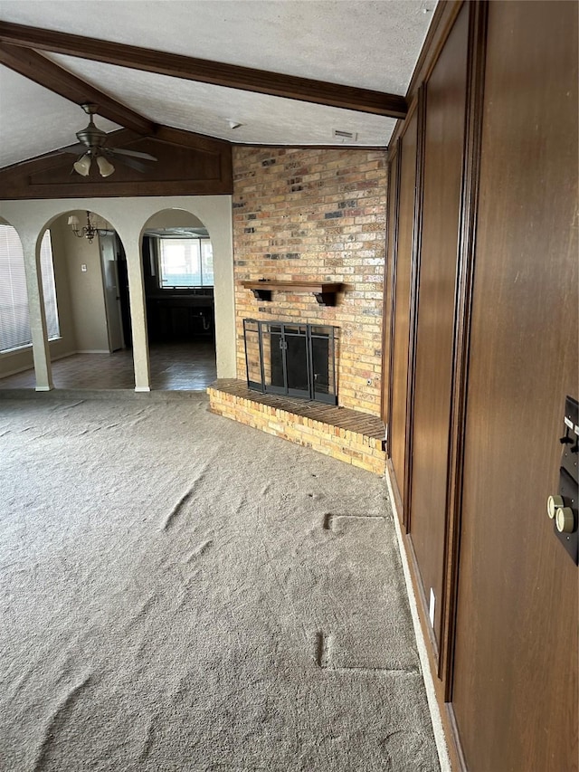 unfurnished living room featuring carpet flooring, ceiling fan, lofted ceiling with beams, a fireplace, and arched walkways