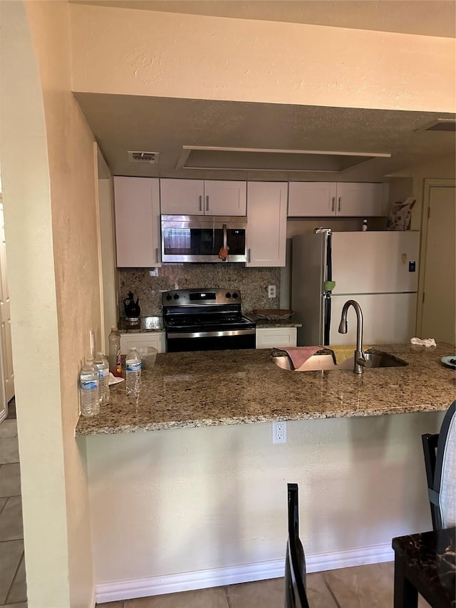 kitchen with a sink, tile patterned flooring, stone countertops, stainless steel appliances, and backsplash