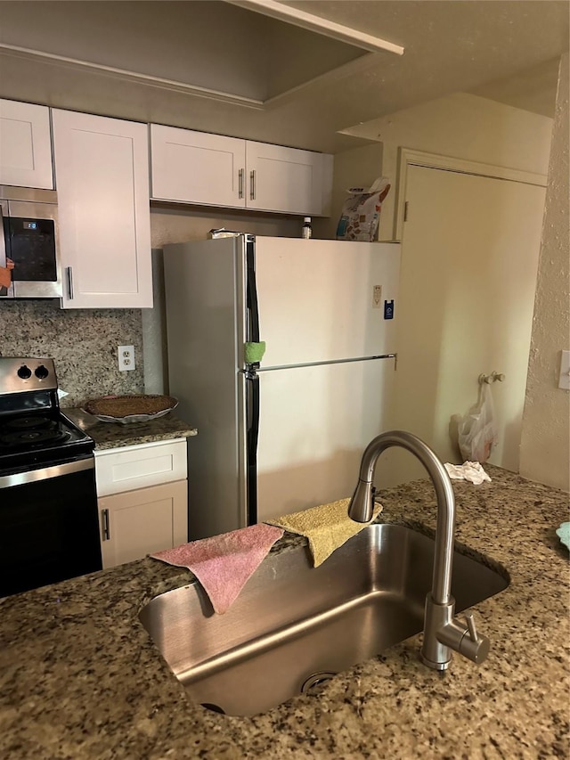 kitchen with a sink, stone counters, stainless steel appliances, and white cabinetry